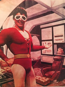 In this vintage photo, CCL volunteer Mark Taylor is dressed as DC superhero Plastic Man, whom he played on television in the 1980s. He wears a red, long sleeve leotard and large, white, goggle style glasses.