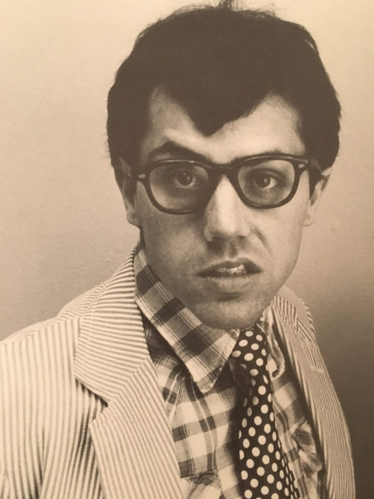 A vintage photo of CCL volunteer Mark Taylor early in his acting and comedy career. He wears a striped suit, a checkered button up, and a polka dotted tie, pouting his lip goofily at the camera.