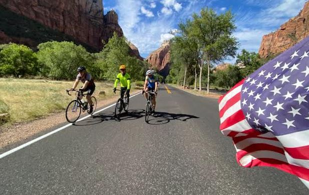 Pedaling for a purpose: Bike tour raises awareness for climate change; Utah bicyclists ride their bikes down the road with an American flag