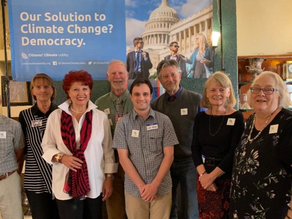 Eight CCL volunteers pose for a picture indoors, in front of a CCL banner that reads "Our solution to climate change? Democracy."