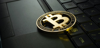 a physical, yellow, metallic Bitcoin logo sitting on a laptop