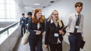 Two young women and a young man wear business professional clothing and lanyards, walking down a hallway