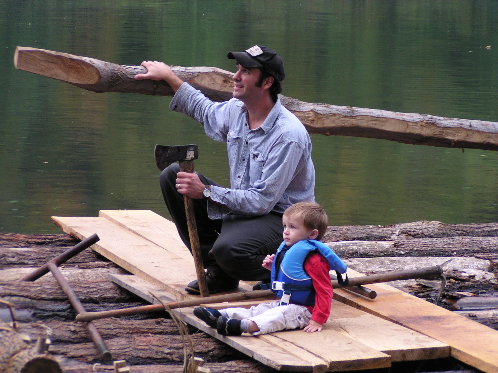 A man and a young child riding a log raft on the Susquehanna River