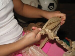 A close-up image shows a child's hands braiding plastic bags