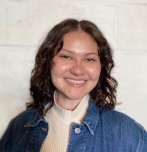 A young smiling woman wears a turtleneck sweater and collared shirt