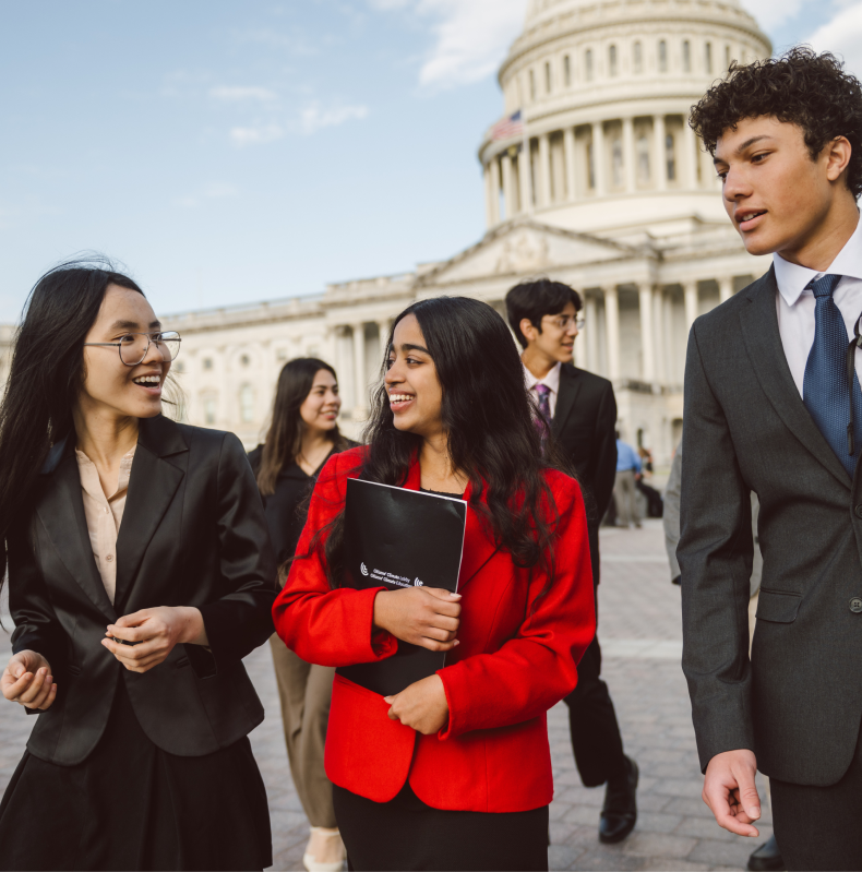 A diverse group of young professionals in business attire walking and conversing outside the U.S. Capitol building, showcasing collaboration and advocacy efforts.