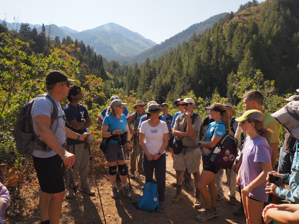 A candid photo of a group of hikers talking, with forested mountains visible in the background.