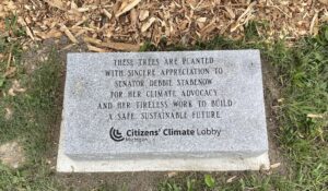 A gray stone plaque reads: These trees are planted with sincere appreciation to Senator Debbie Stabenow for her climate advocacy and her tireless work to build a safe, sustainable future.