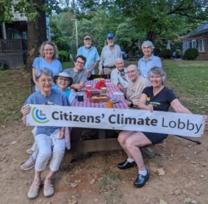 Smiling people sit around a picnic bench holding a sign with the Citizens' Climate Lobby name and logo.